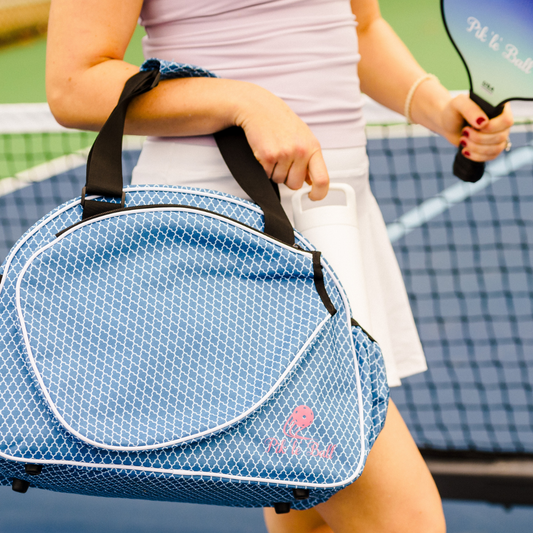 Person holding a blue duffel bag with a pink logo on a tennis court