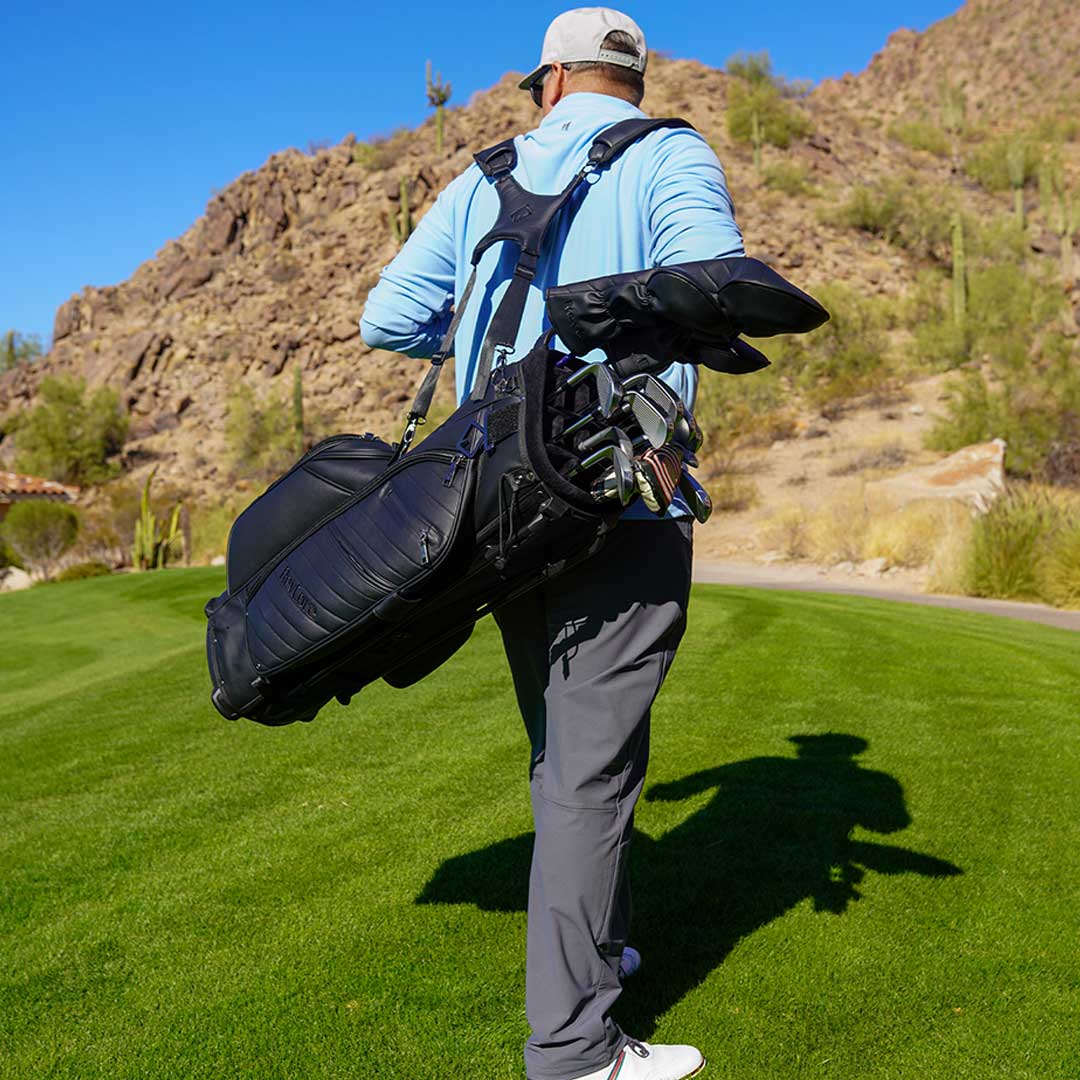 Man carrying a golf bag on a golf course with mountains in the background