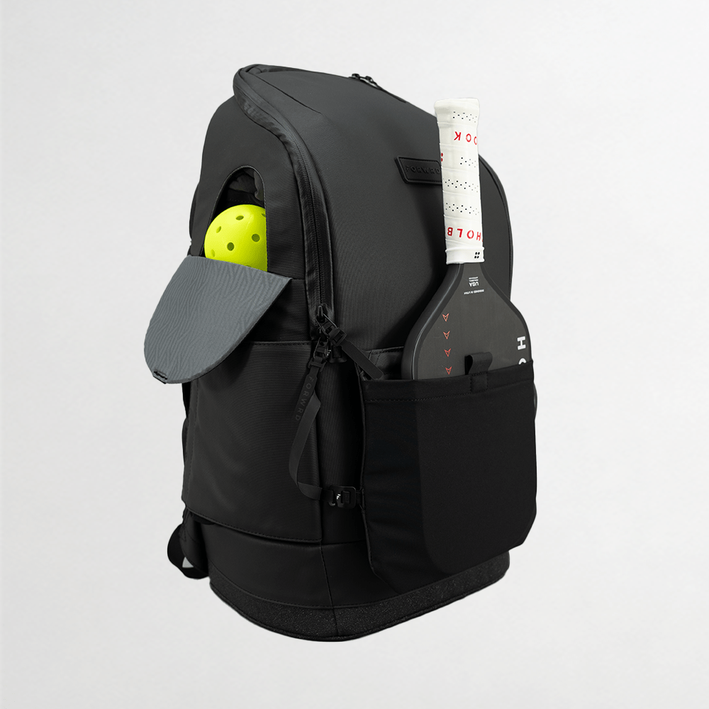 Black backpack with a yellow ball and gray paddle in compartments on a light gray background
