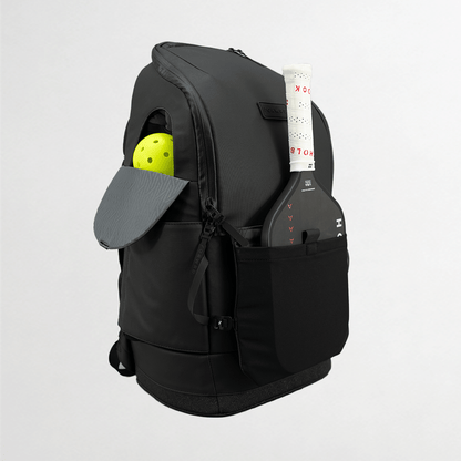 Black backpack with a yellow ball and gray paddle in compartments on a light gray background