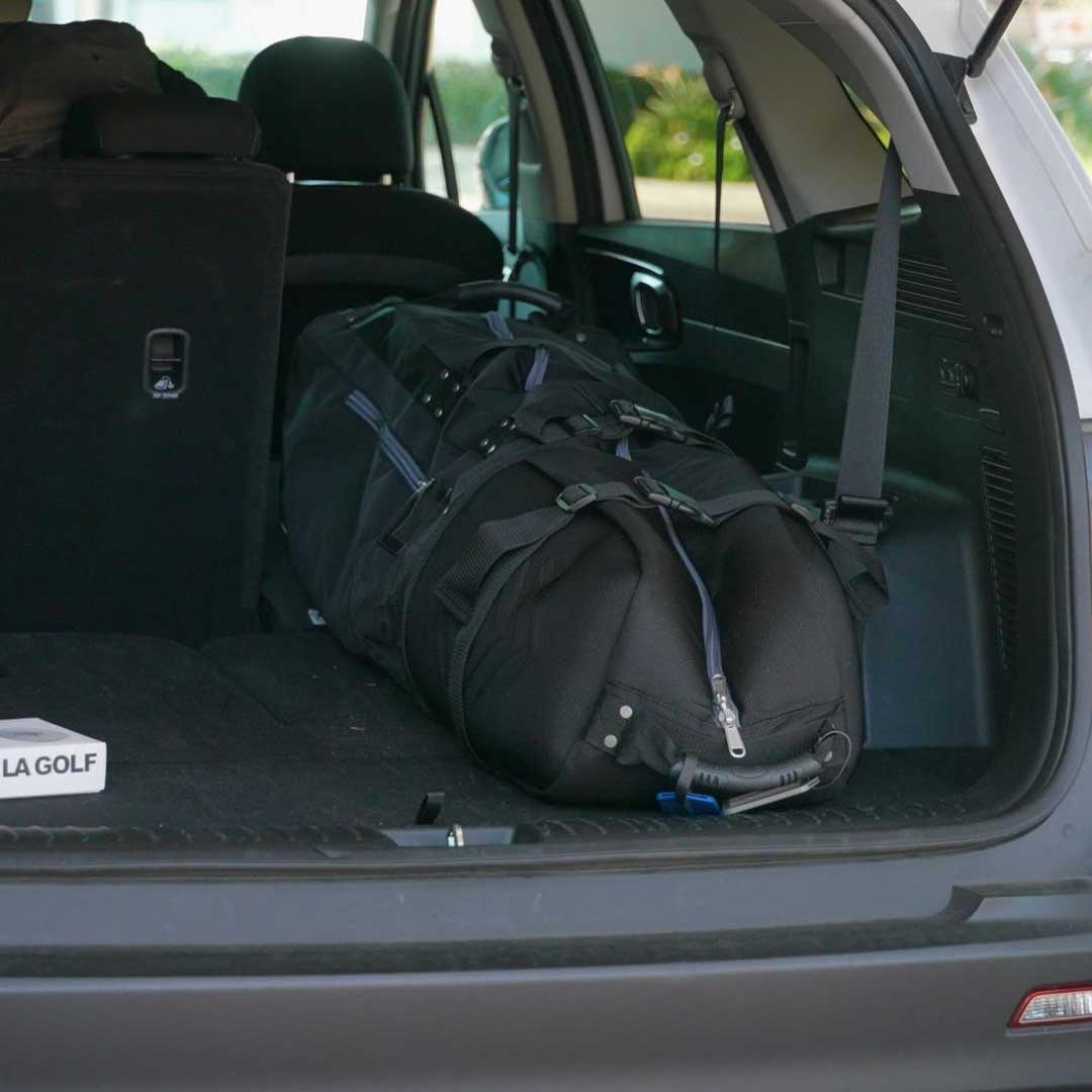 Black golf bag in the trunk of a car with a visible brand logo.