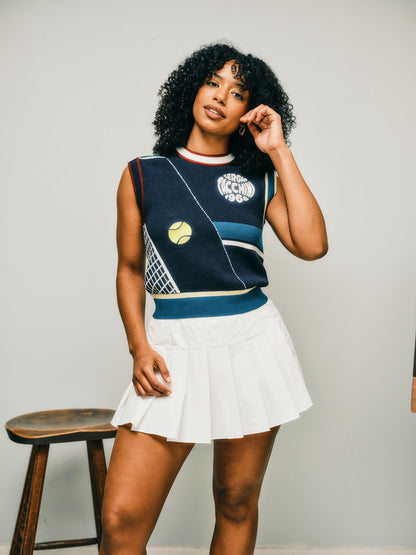 Woman wearing a sleeveless tennis top with geometric patterns and a white skirt against a plain background