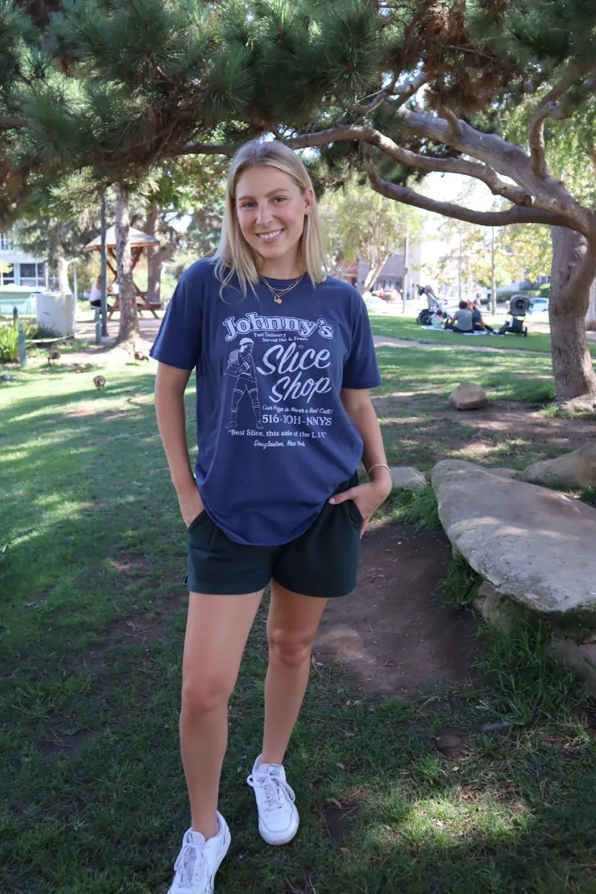 Person wearing a blue t-shirt with text standing in a park