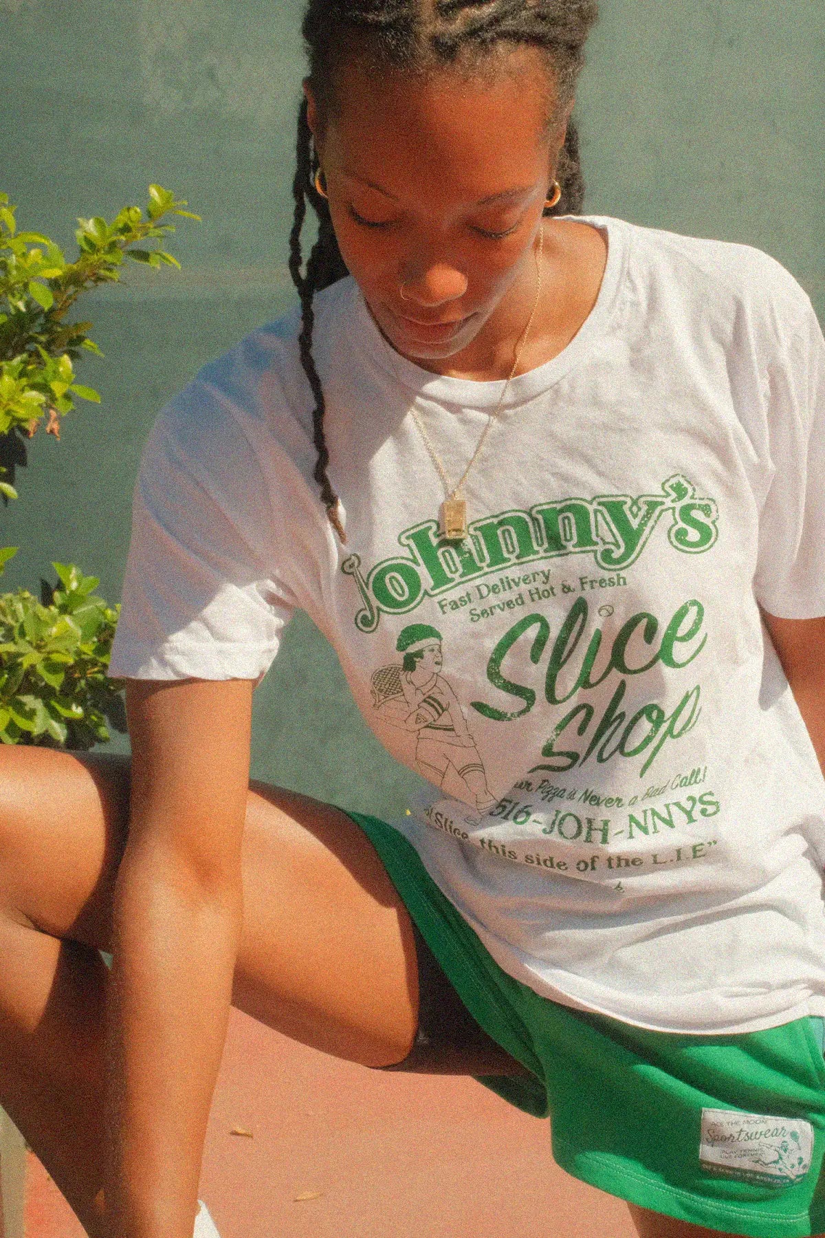 Person wearing a white t-shirt with 'Johnny's Slice Shop' text, sitting outdoors.