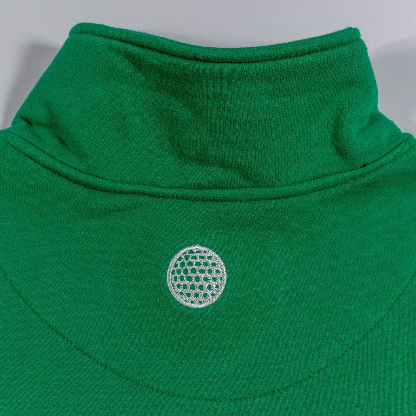 Close-up of a green garment with a white embroidered design on a gray background