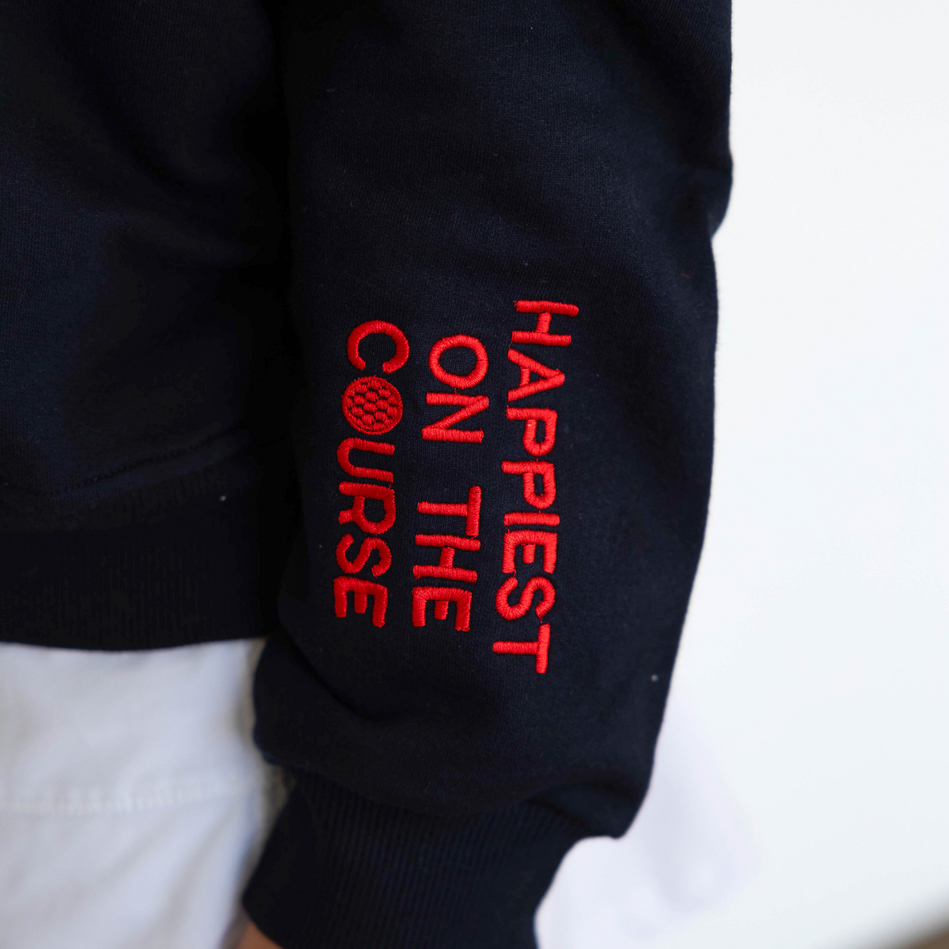 Black sweatshirt with red text 'Happiest on the Course' on a white background