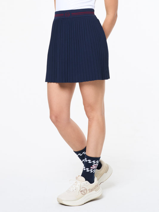 Person wearing a navy pleated skirt, white sneakers, and patterned socks on a white background