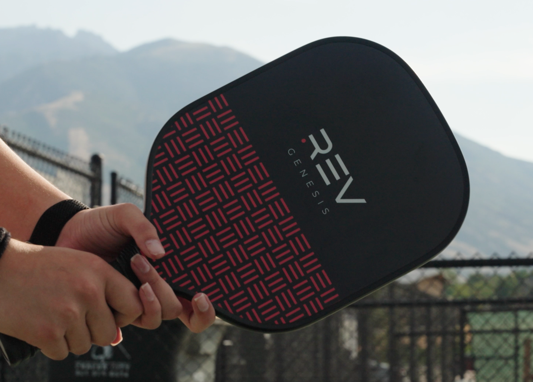 Person holding a pickleball paddle with 'REV' branding against a mountainous background