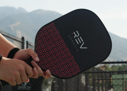 Person holding a pickleball paddle with 'REV' branding against a mountainous background
