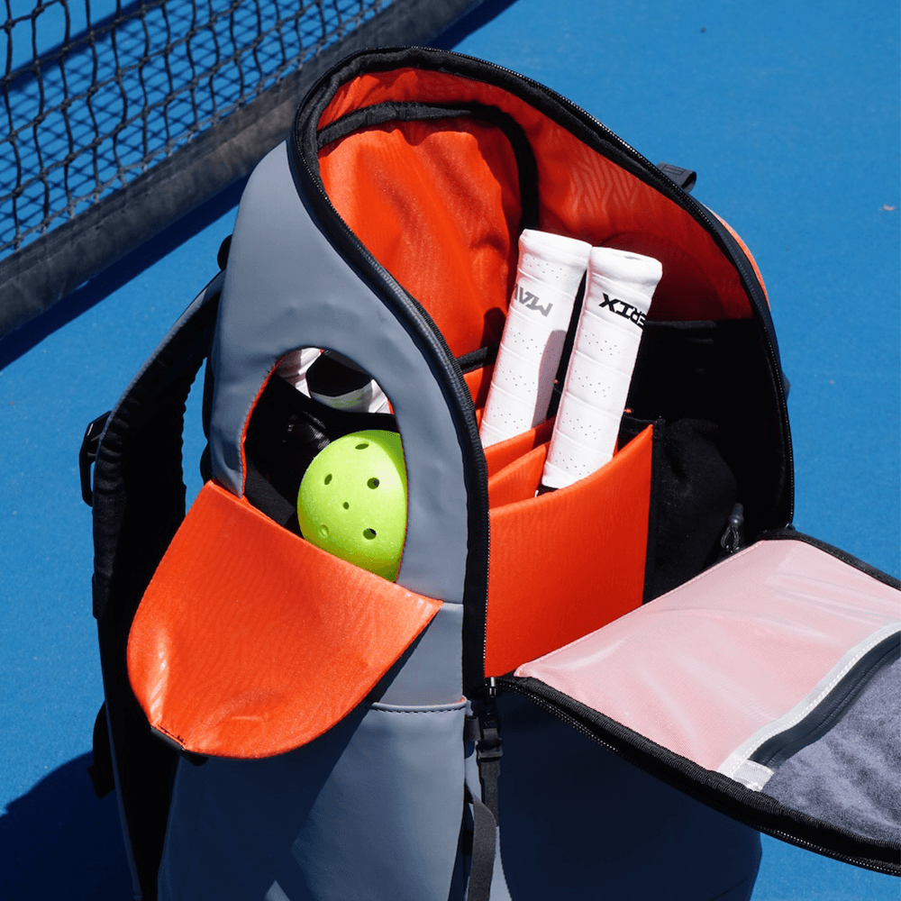 Open backpack on a tennis court with sports equipment inside