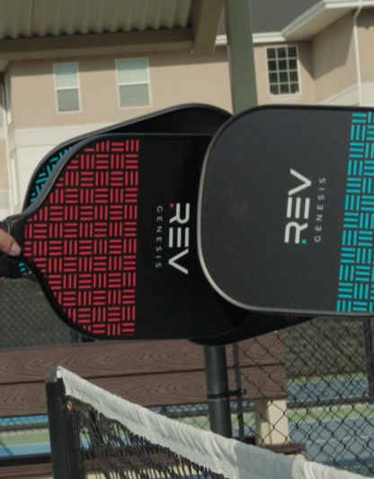 Pickleball paddle with 'REV' branding held by a person outdoors.