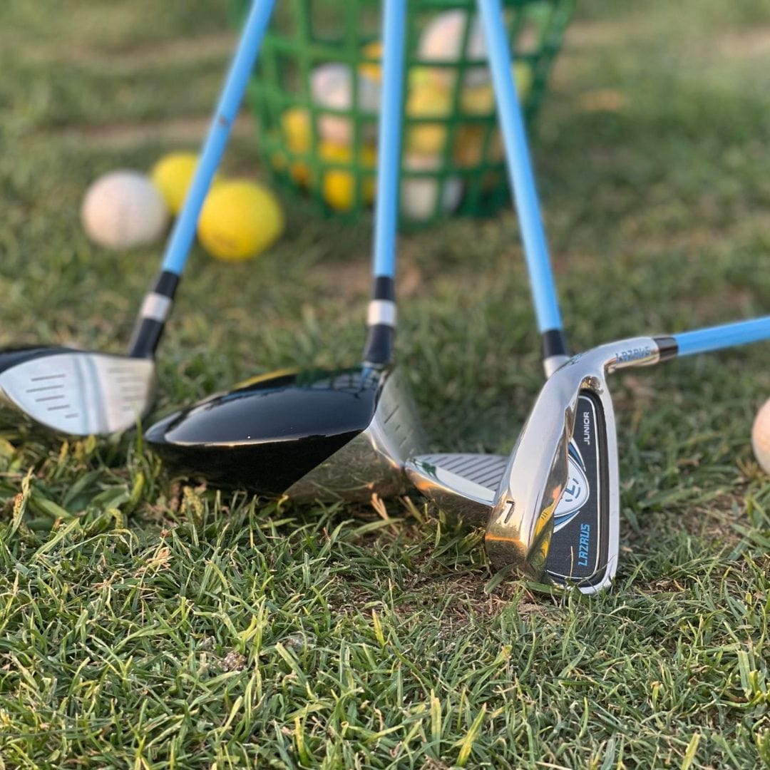 Golf clubs for kids on grass with golf balls and a basket in the background