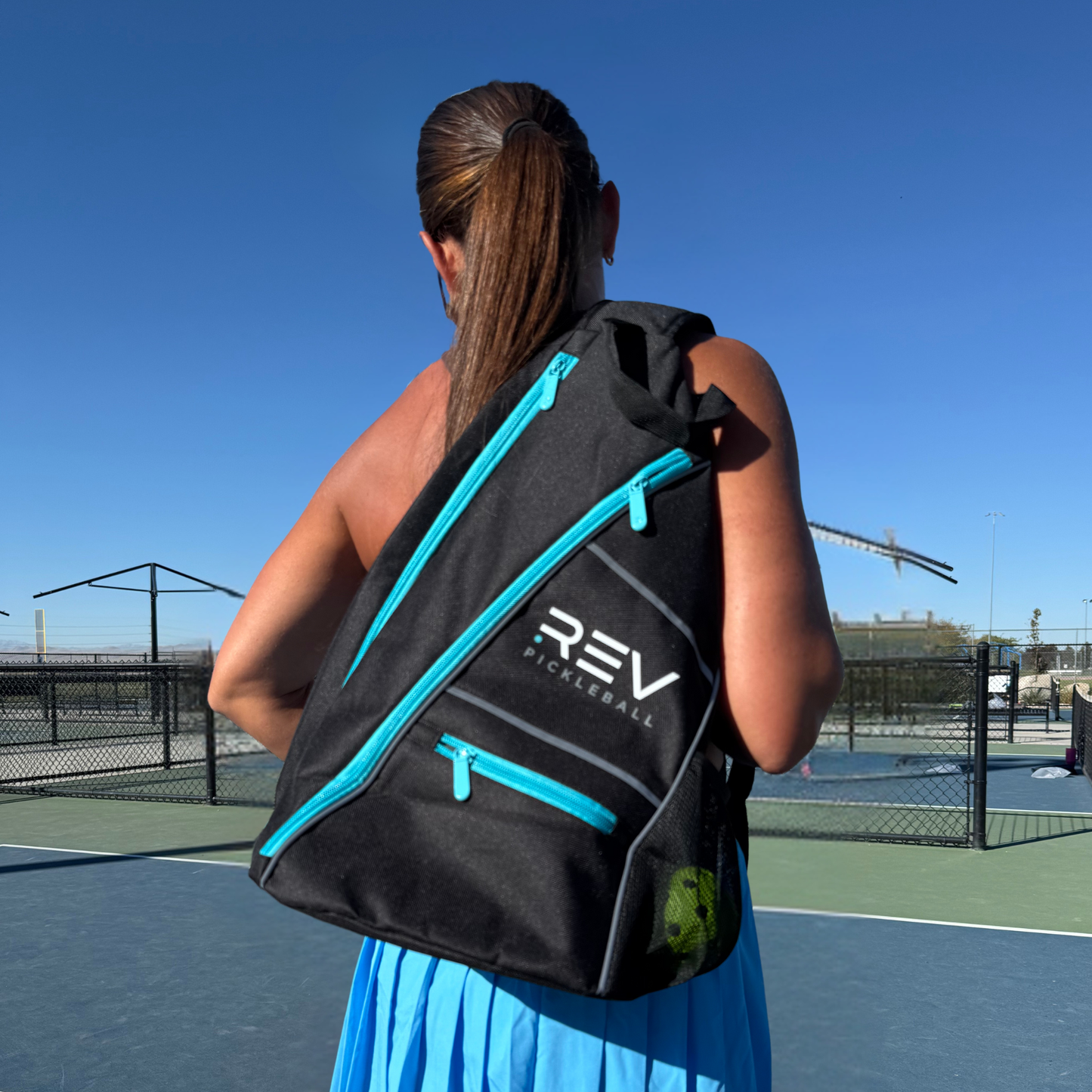 Person carrying a black and blue REV pickleball bag on a tennis court