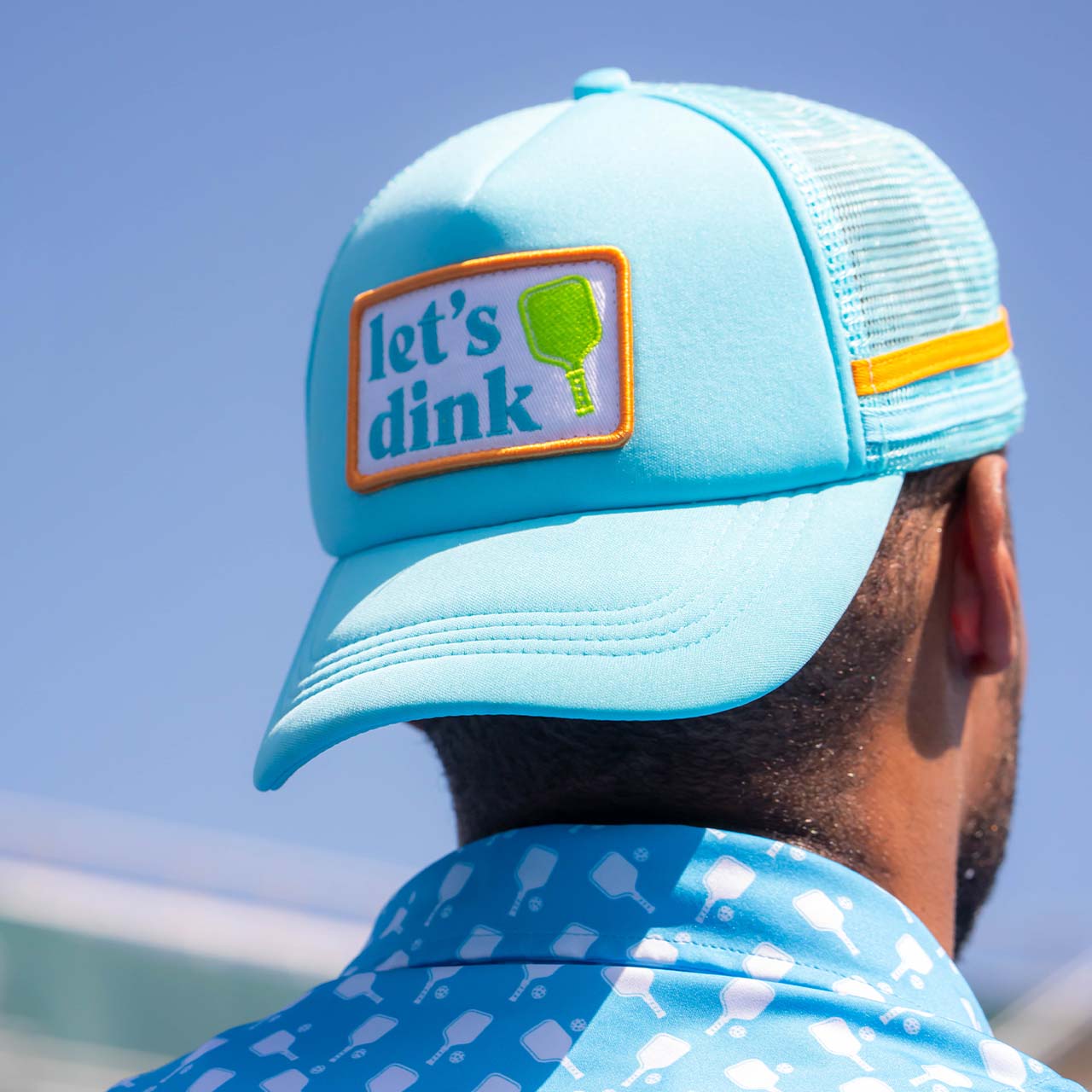Light blue cap with 'let's dink' patch worn by a person against a clear blue sky.