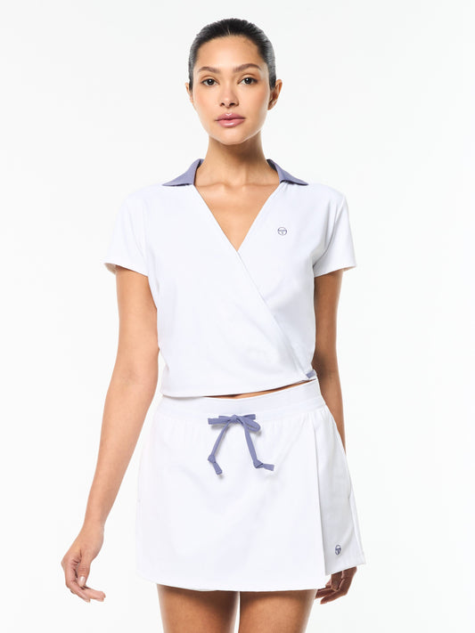 Woman wearing a white tennis outfit with a purple bow on a white background