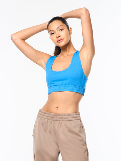 Woman wearing a blue sports bra and beige pants on a white background